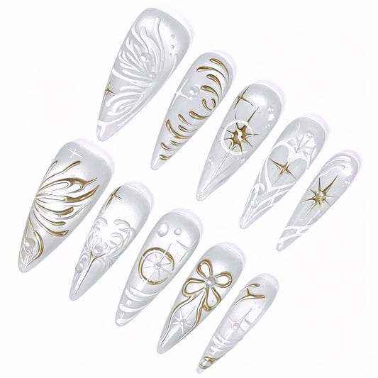 Angled detail of pearl-white stiletto nails with gold stars, bow and raised white patterns