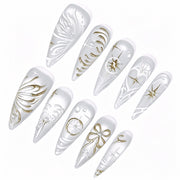 Angled detail of pearl-white stiletto nails with gold stars, bow and raised white patterns